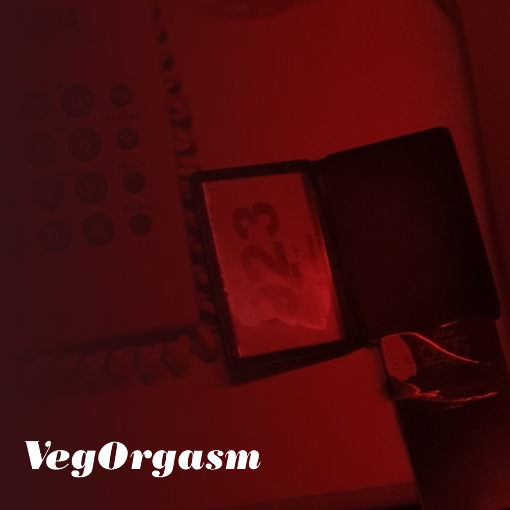 A nightstand view under harsh red lighting, showing a landline telephone, a glass coaster or ashtray, and a small, open black booklet with a white '923' illuminated on the right page.